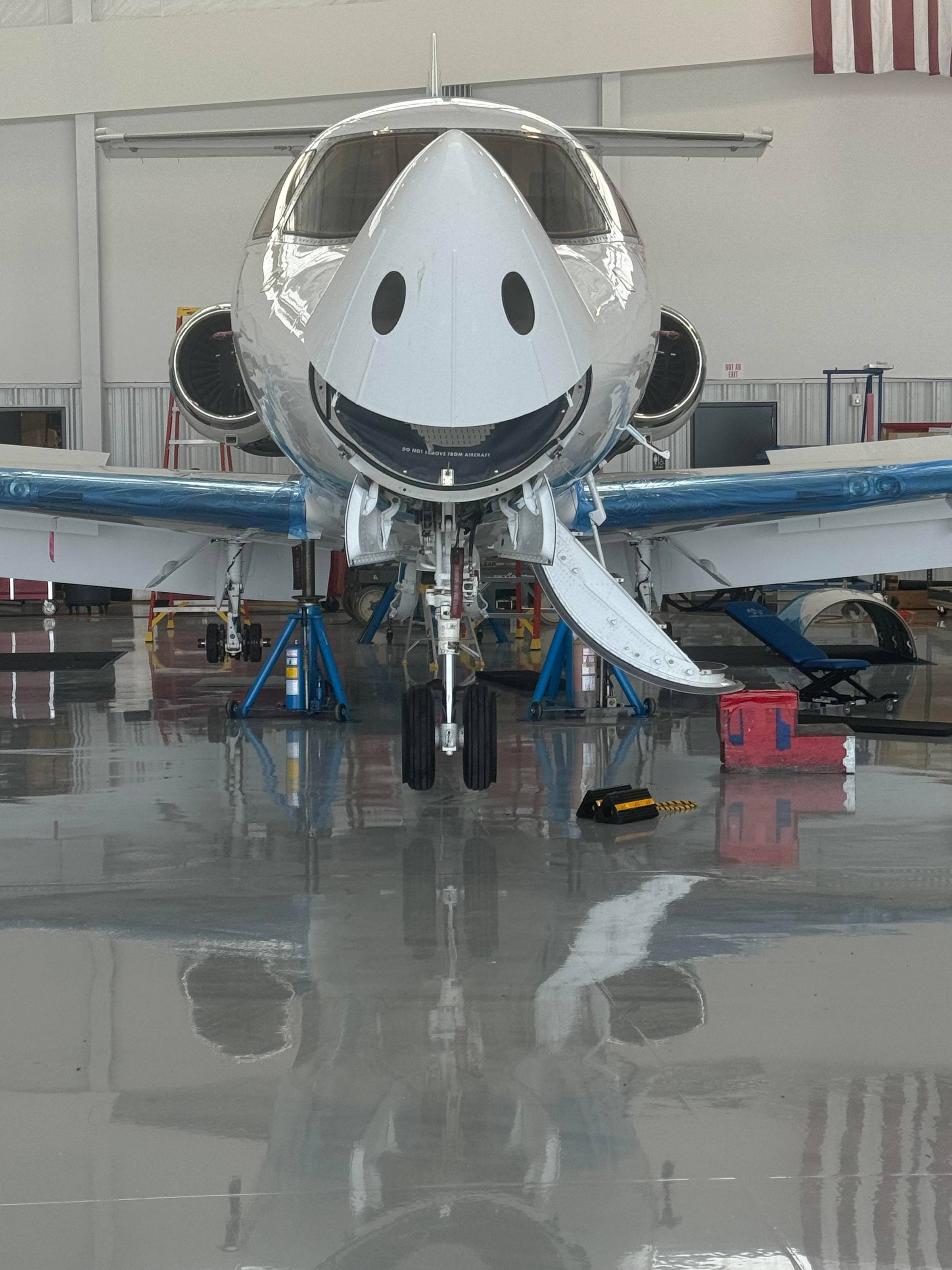 Hawker 400 on jacks in the hangar, head-on, with a smiling face on its nose and the airstair down